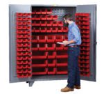 A man confidently stands before a sleek gray Little Giant High Capacity Storage Bin Cabinet, wearing a blue shirt, jeans, and brown shoes. Holding a clipboard, he inspects the neatly arranged multiple red bins inside the cabinet.