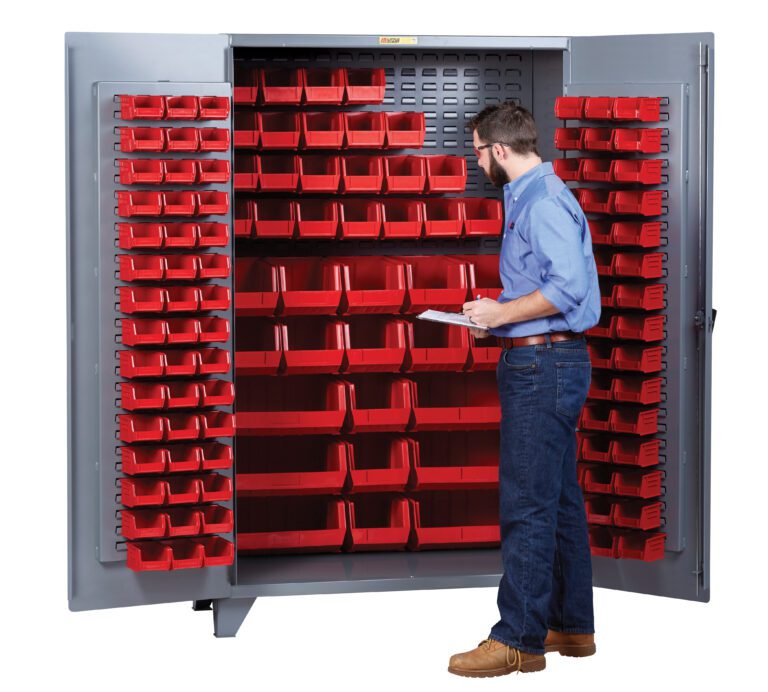 A man confidently stands before a sleek gray Little Giant High Capacity Storage Bin Cabinet, wearing a blue shirt, jeans, and brown shoes. Holding a clipboard, he inspects the neatly arranged multiple red bins inside the cabinet.