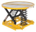 The Vestil Spring Scissor Table 4,500 Lb Cap is a yellow industrial lift table with a round platform and black spring mechanism. Expertly designed for ergonomic lifting and positioning tasks, it is ideal for warehouses or assembly lines.