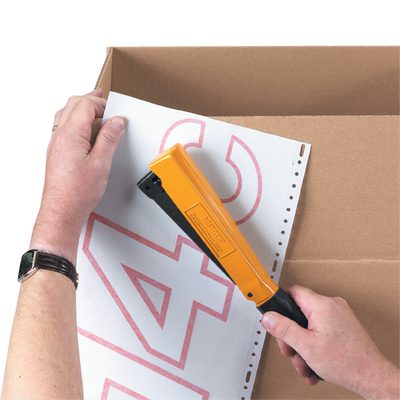 ST127.jpg Using a Bostitch Stapling Hammer, someone skillfully tacks perforated paper with red numbers onto a cardboard box, steadying the paper with their left hand and ensuring precise placement with their right.