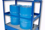 Two blue metal barrels are secured on a gray grate within a sturdy blue storage rack enhanced by the Vestil Drum Pallet - Security Bar Option, offering extra stabilization with horizontal bars.