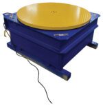 The Vestil Chain Driven Ac Carousel 4K Lb 48 In Dia features a sturdy blue design with a textured yellow circular top, flat square base, and side power cord, ideal for heavy-duty applications.