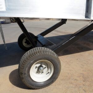 Close-up of Vestil Pneumatic Tire Option on a metal trailer: Two rubber tires with white rims are connected by black metal braces, with a chain hanging from the side, all on a concrete surface.