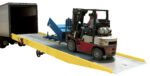 A forklift operator is maneuvering a red and gray forklift up a Vestil Yellow Curb Paint Option ramp, seamlessly blending into the plain white background. The efficient forklift carries blue equipment into the rear of a large truck.