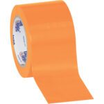 A roll of the 3 x 36 yds. Orange (3 Pack) Tape Logic® Solid Vinyl Safety Tape partially unrolls to reveal its vibrant hue, while the branded core highlights its reliability and safety for high-visibility uses.