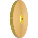 The tan 3M™ 465XL Adhesive Transfer Tape roll (1/2 x 60 yds.) features green and black text on its side and a yellow core with red letters. It stands upright against a white background, ready for any task.