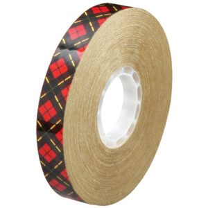 The 3/4 x 36 yds. (6 Pack) 3M™ 924 Adhesive Transfer Tape features tightly wound transparent tape on a brown spool with a white core and a striking red and black plaid outer wrap featuring yellow stripes.