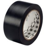 The 2 x 36 yds. Black 3M General Purpose Vinyl Tape 764, available in cases of 24, is partially unrolled, showcasing its glossy finish and white inner core with printed text and a plaid pattern.