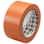 A roll of 2 x 36 yds. Orange 3M General Purpose Vinyl Tape 764, included in a 6 Pack, is angled slightly. It has a white inner core with a black plaid pattern and text, showcasing its new, smooth surface.