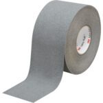 A 4 x 60 roll of Gray 3M™ Safety-Walk™ Tape - 370, partly unrolled, displays its textured surface. Upright, it shows the inner cardboard core with a small red logo inside.