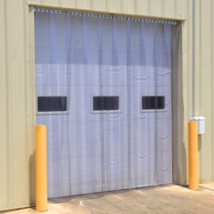A Vestil Vinyl Strip Door 0.16 In Full 168 X 240 is installed in a pale yellow metal building garage. The semi-transparent door has three rectangular windows and is flanked by two yellow bollards, striking a balance between sturdiness and a welcoming appearance.