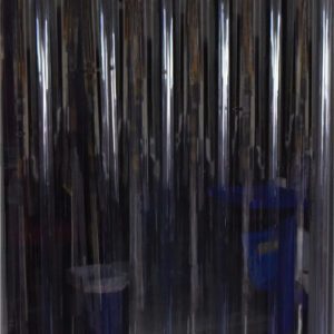 Clear strip curtains, similar to those in the Vestil Vinyl Strip Door 0.16 In Std Wall 96 X 108, hang from a metallic rail, providing visibility while creating a barrier between spaces. Industrial equipment and storage items are partially visible behind the transparent strips.