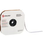 A roll of 1 3/8 White VELCRO® Brand Tape with individual dots (600/case) comes in a brown cardboard dispenser, displaying the Velcro logo and brand details on the front, with the hook tape extending from the side.