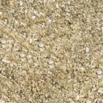 Close-up of MH-USA Vermiculite 4A - Extra Coarse, surrounded by beige-grain sand and assorted pebbles. It has a rough texture and irregular particles, creating a natural earthy look.