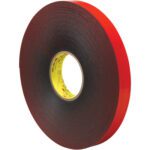 A 1 x 5 yds. roll of Gray 3M™ 4611 VHB™ Tape is displayed edge-up, showing black foam with a red backing. The encased tape with a textured look winds tightly around a yellow core featuring printed text, highlighting its versatile adhesive properties.