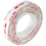 A roll of 1 x 5 yds. White 3M™ 4920 VHB™ Tape features red text on a white backing, is translucent, with the adhesive inward and brand details in red on the outside.
