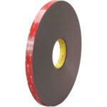 A large roll of 3/4 x 5 yds. Black 3M™ 4947F VHB™ Tape (1 Roll/Case) stands upright against a pristine white background, featuring a red backing, white branding text, and the yellow inner core subtly visible.