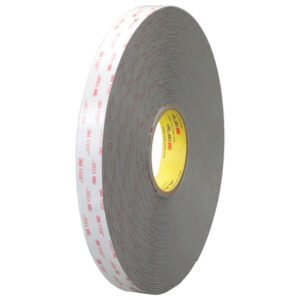 The 3/4 x 5 yds. Gray 3M™ 4956 VHB™ Tape (1 Roll/Case) is shown upright, highlighting its thickness with coiled layers. It features a protective white backing and an inner core with red text and the brand logo.