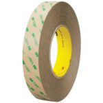 The 2 x 5 yds. Clear 3M™ F9473PC VHB™ Tape roll has a brown outer layer with green 3M VHB text and a yellow inner layer, slightly tilted to reveal its sturdy design, width, and diameter.