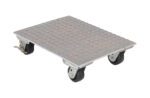 The Vestil Aluminum Plate Dolly 1.2K Lb Cap 18X24 is a flat, metal platform with a diamond plate surface and four black swivel wheels, designed for easy transport of heavy items. It includes a locking mechanism on one wheel for added stability.