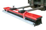 The Vestil Valusweep Series Magnet 4 Foot attachment, with black bristles, mounts on forklift forks for sweeping large areas like warehouses or parking lots. It includes two securing knobs for stability.