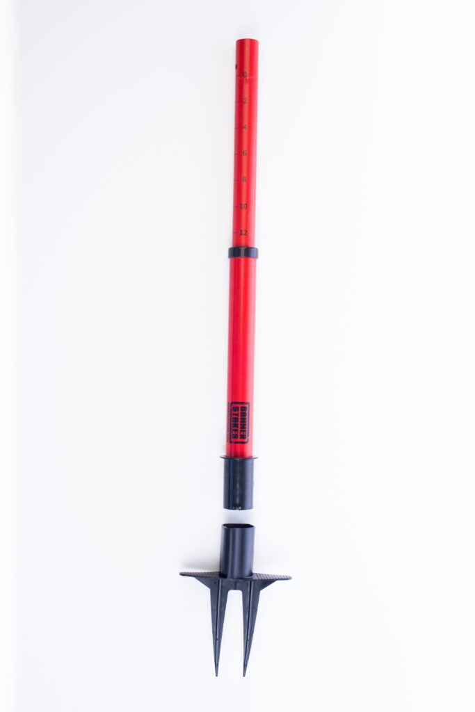 This Vestil Web Barrier Stake 42 in red is a gardening tool with a telescopic handle and retractable metal prongs, ideal for aerating soil. The segmented design allows adjustable length, set against a plain white background.