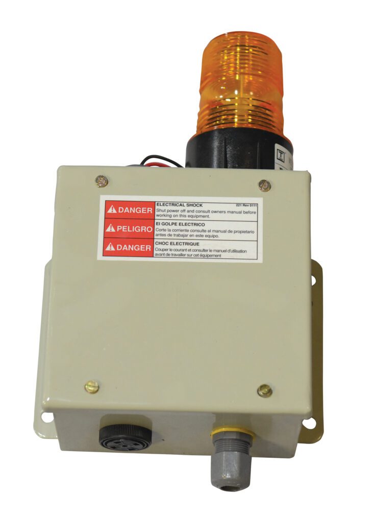 The Vestil Dock Lift comes with a beige box featuring red and white warning labels in English and Spanish, an orange cylindrical light on top, a black dial, metal connector, and the option for a beeper & strobe to enhance safety against electric shock and danger.