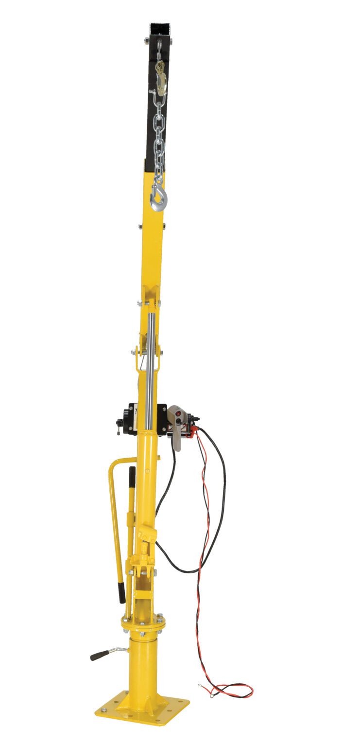 The yellow Vestil Winch Operated Truck Jib Crane - DC features a vertical arm, hydraulic lever, chain, and attached wires. Its designed for lifting heavy objects and has a sturdy base for stability.