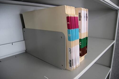 A row of color-coded manila file folders with labeled tabs stands on a metal shelf divider. The folders have labels with letters and colors, sorted alphabetically from E to H, against an empty gray shelf background.