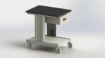 A mobile metal cart with four caster wheels, featuring a black rectangular tabletop and a small square drawer underneath. The base is metallic with a clean, industrial design. The cart is set against a plain white background.
