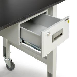 A white metal drawer is open beneath a black tabletop. The drawer is part of a wheeled worktable. The drawer has a lock and a handle. The table has a sturdy metal leg on a caster wheel for mobility.