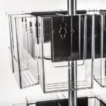 A close-up showcases the Vulcan CIRC 12 CLEAR 11 POCK 3 ROTATORS, a rotating metal stand with empty clear pockets ideal for brochures or cards, set against a plain white background.