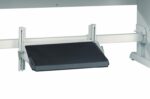 An adjustable footrest attached to the framework of a desk, featuring a flat black surface and a metallic structure. The footrest can be angled and positioned according to comfort preferences. The background is plain white.