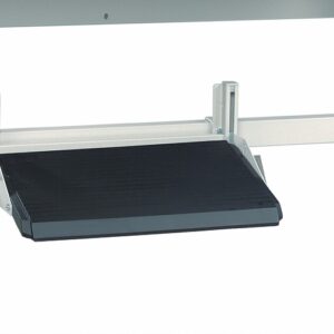 An adjustable footrest attached to the framework of a desk, featuring a flat black surface and a metallic structure. The footrest can be angled and positioned according to comfort preferences. The background is plain white.