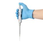 A hand in a blue glove holds a white pipette against a plain background.