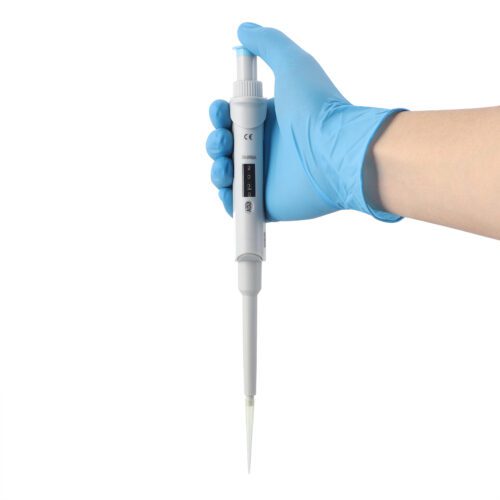 A gloved hand holds a white pipette against a white background. The pipette has measurement markings, a digital display, and a tip ready for liquid transfer, typical in laboratory settings.
