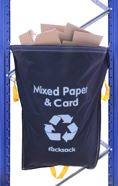 RS_01.jpg A blue recycling bag labeled Mixed Paper & Card with a recycling symbol is attached to a metal rack. The bag is filled with cardboard. Yellow handles are visible on the sides and bottom.