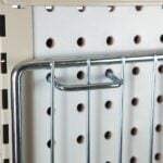 A close-up of a metal grid with a Vulcan U-HOOK DISPLAY ACCESSORY (25 per bag) on a beige perforated pegboard highlights the potential for organization and streamlined display setups through evenly spaced holes and secure grid arrangement.
