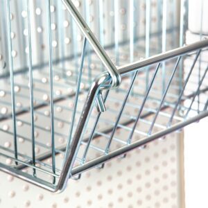 A Vulcan WIRE 12 OEB DIVIDE shopping basket hangs on a pegboard wall. The shiny silver wires form a neat grid pattern with visible angled edges, and the boards spaced holes are ideal for organization. (10 per carton).