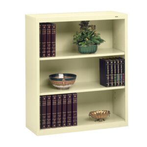 A cream-colored three-shelf bookcase with decorative items. The top shelf has a green potted plant. The middle shelf features a decorative bowl and books. The bottom shelf holds several books and a small decorative bowl.