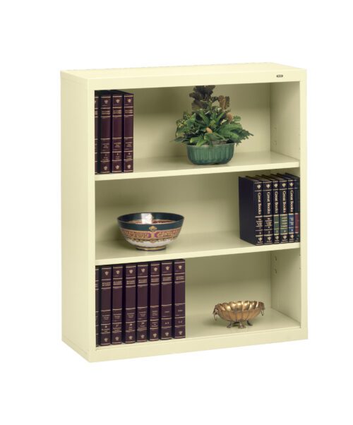 A cream-colored three-shelf bookcase with decorative items. The top shelf has a green potted plant. The middle shelf features a decorative bowl and books. The bottom shelf holds several books and a small decorative bowl.