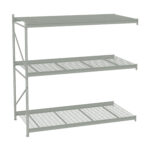 Metal shelving unit with four tiers, including three grated shelves and one solid top shelf. The structure has a light gray finish and is designed for industrial or garage storage. The unit has a minimalist and utilitarian design.