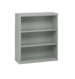 A light gray metal bookshelf with three adjustable shelves. The design is simple and utilitarian, suitable for office or home use. The bookshelf is empty and stands against a plain white background.