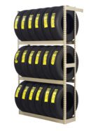 A shelving unit holds three rows of tires, each labeled with yellow tags. The tires are neatly organized and stacked, indicating a storage or retail display. The shelving is a simple metal frame structure.