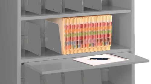 A gray metal cabinet with three shelves containing organized file folders. The middle shelf displays folders with multicolored labels. A pull-out shelf has a notepad and a pen on it.