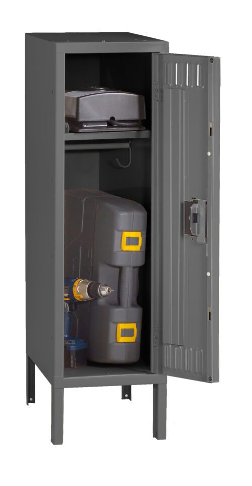 A tall, grey metal cabinet with an open door revealing a power drill and tool case on the bottom shelf, and a closed case on the upper shelf. The cabinet stands on four legs.