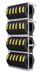 A metal shelving unit holds three rows of stacked black tires. Each tire has a yellow label on its tread, indicating specifications or pricing. The shelves are evenly spaced, and the setup appears organized and clean.