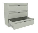 A light gray, metal filing cabinet with three drawers is shown. The top two drawers are closed, while the bottom drawer is open, revealing an empty interior. The cabinet is viewed at a slight angle from the front.
