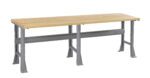 A long workbench with a light wood tabletop and sturdy gray metal legs. The design features a support beam running horizontally between the legs for additional stability. The table has a simple and industrial appearance.