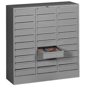 A gray metal storage cabinet with multiple small drawers arranged in rows. One drawer is partially open, containing magazines.